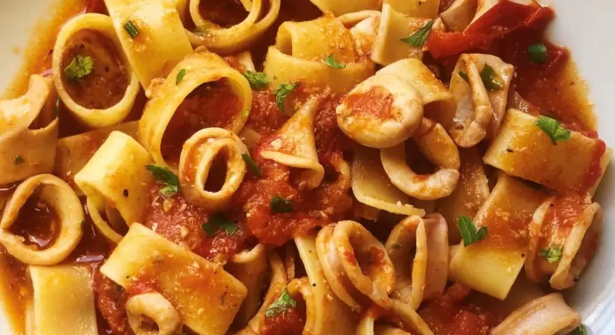 Pasta con calamares, un plato italiano lleno de sabor. Los calamares se mezclan con trozos de tomate y perejil fresco, creando una deliciosa combinación.