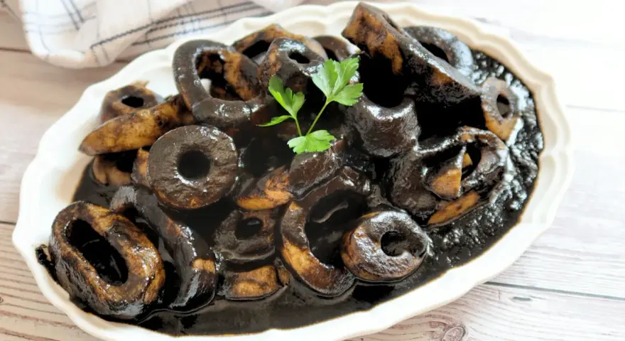Calamares en su tinta, un plato tradicional español, servido en una fuente blanca con perejil fresco.