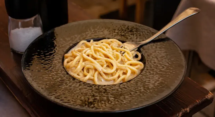 Pyszne cacio e pepe na czarnym talerzu, z widocznym młynkiem do pieprzu i solniczką w tle.