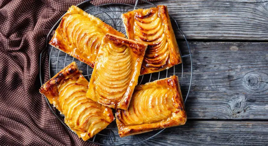Deliziosi dolci con pasta sfoglia e mele caramellate, disposti su una gratella, su un tavolo di legno rustico.