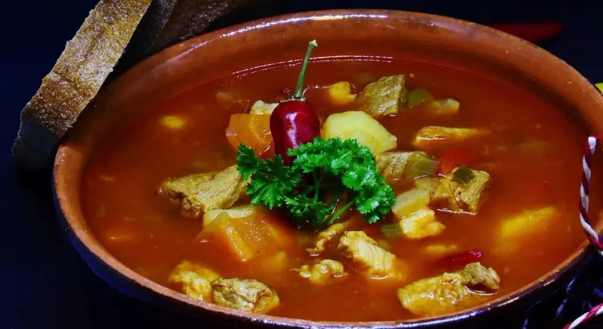 Pyszna zupa gulaszowa Ewy Wachowicz z kawałkami mięsa, ziemniaków i papryki, udekorowana papryczką chili i natką pietruszki. Podana z chlebem.