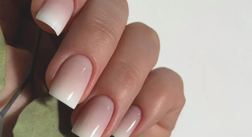 Mano con unghie curate e un effetto sfumato bianco e rosa, un esempio di nail art semplici ed eleganti.