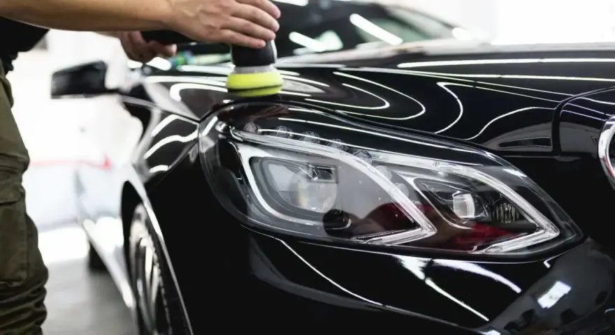 A person uses a polisher to wax a shiny black car, bringing out its deep gloss.