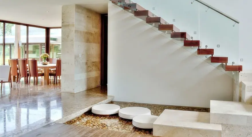 Escalera de madera flotante con barandilla de cristal. Ideas para decorar una escalera de madera con un estanque de guijarros y piedras.