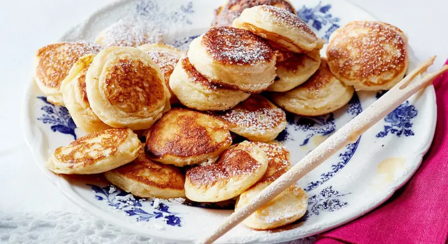 Ein Teller voller goldbrauner Poffertjes, bestäubt mit Puderzucker. Dieses Poffertjes Rezept ist ein Genuss!