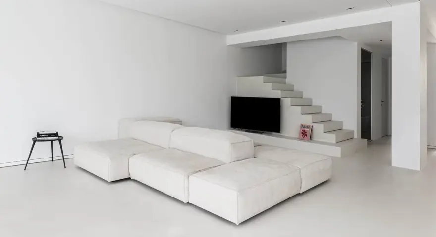 Soggiorno minimalista con divano modulare bianco e pavimento in resina lucida. Scale moderne integrano la TV.