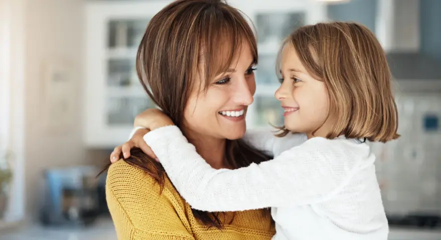 Uśmiechnięta mama i córka przytulają się, emanując ciepłem i bliskością. To kwintesencja rodzicielstwa bliskości.