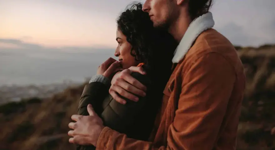 A couple embraces, looking out at a hazy landscape. This image shows how to feel more connected through shared moments and physical closeness.