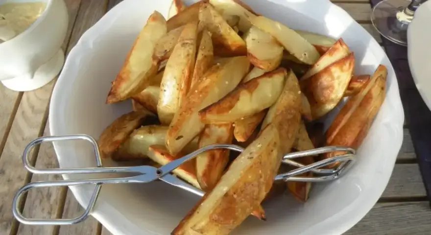 En skål med gyllene klyftpotatis i ugn, redo att serveras med tång.