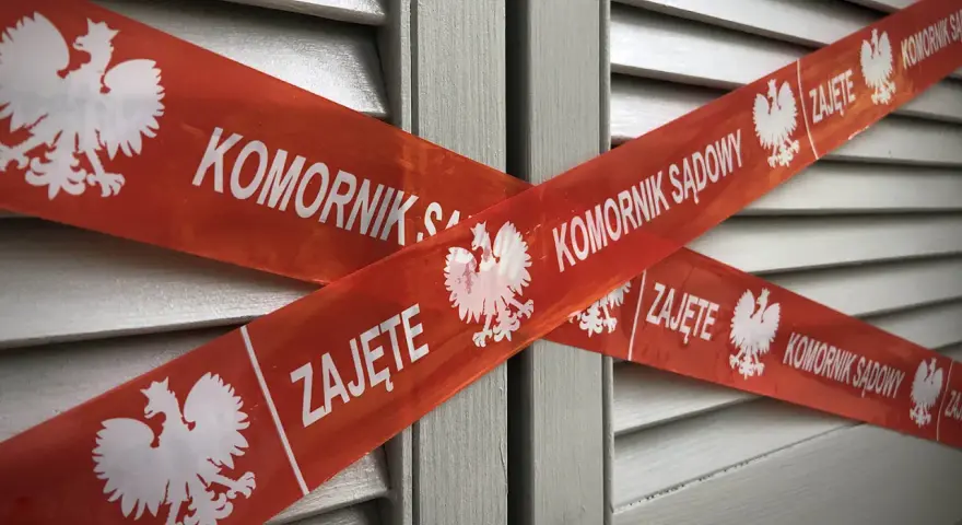 Czerwona taśma z napisem "KOMORNIK SĄDOWY" i godłem Polski krzyżuje się na szarym tle. Nakaz zapłaty w postępowaniu upominawczym a komornik.