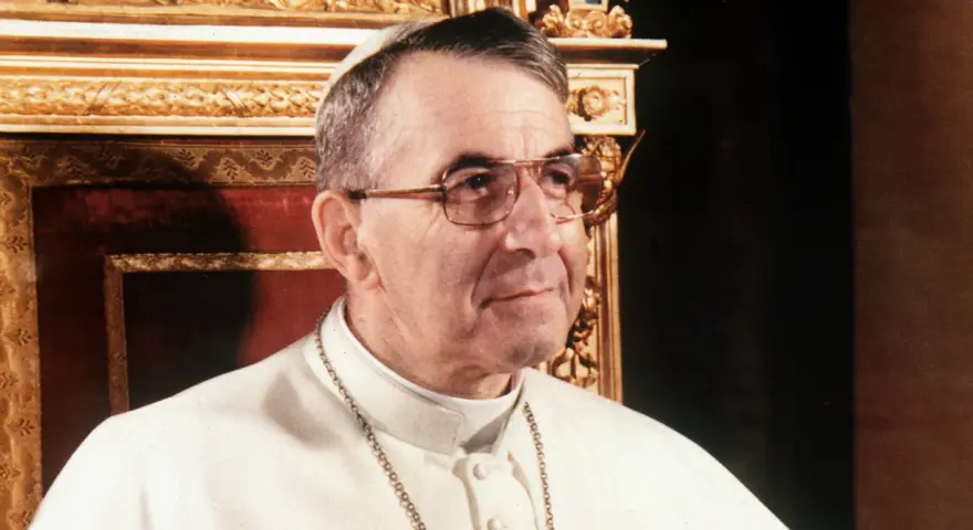 Papież Jan Paweł I, który był papieżem przed Janem Pawłem II, w białej sutannie i okularach.