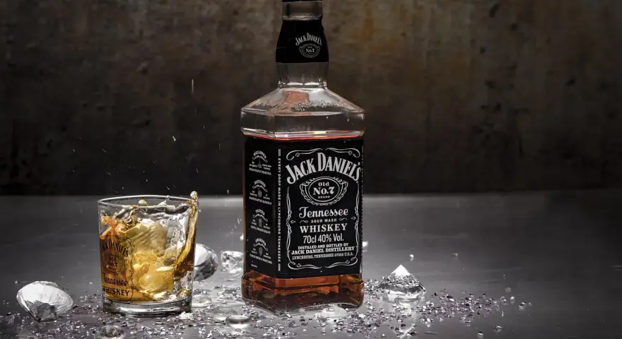 Butelka Jack Daniel's i szklanka z whisky, w której widać plusk. To klasyczny, old fashioned przepis na drinka.