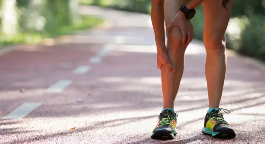 Läuferin hält schmerzendes Knie auf Laufbahn. Knieschmerzen nach Joggen sind ein häufiges Problem.