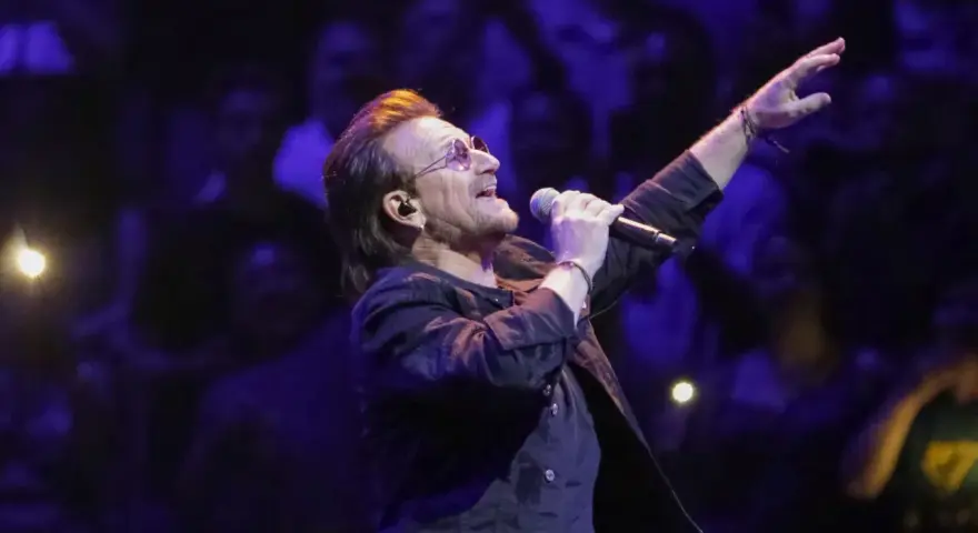 Bono z U2 śpiewa na koncercie, zapowiadając u2 nowa płyta. Tłum w ciemnościach reaguje na jego występ.