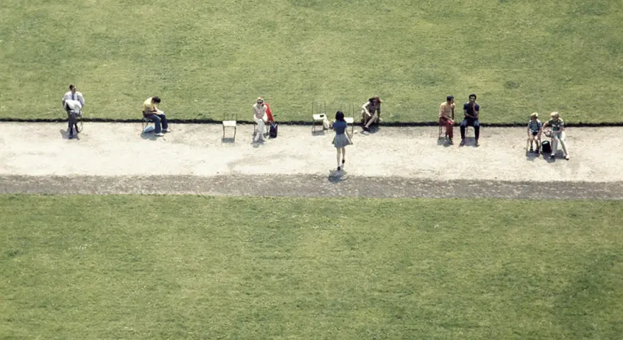 Luigi Ghirri uchwycił ludzi siedzących na krzesłach na tle zielonej trawy.