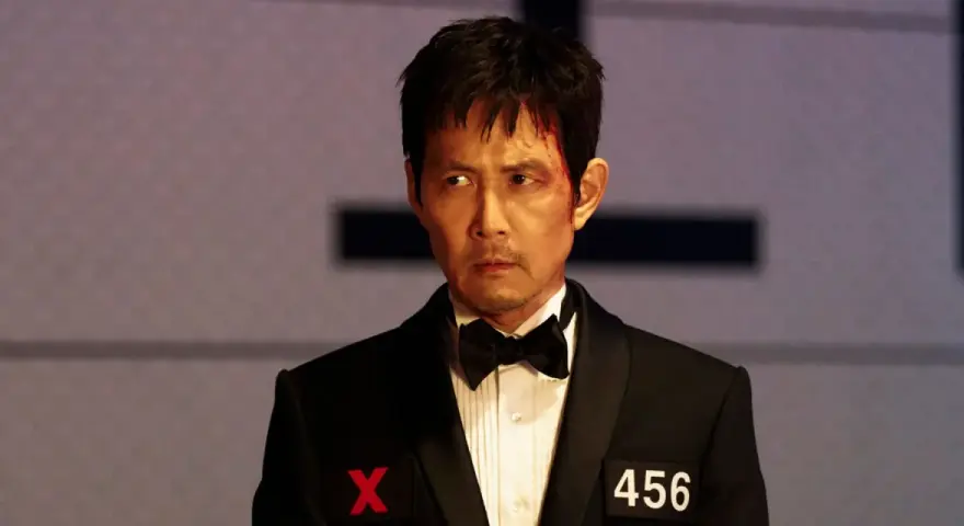 Zraniony Seong Gi-hun w garniturze z numerem 456 i symbolem X, gotowy na kolejne wyzwania w Squid Game sezon 4.