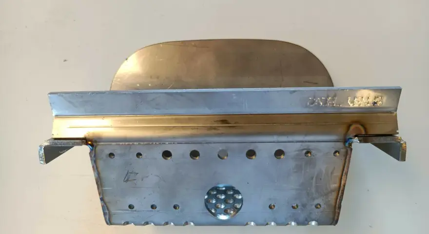 Un abbattitore di fumi per stufe a pellet, realizzato in metallo, con fori e un'area traforata.