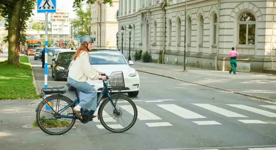 Kvinna på elcykel korsar övergångsställe. Trafik och byggnader i bakgrunden. Elcykel regler är viktiga för säkerheten.