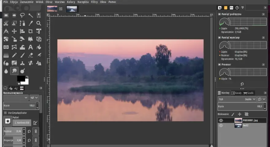 Mglisty poranek nad rzeką, edytowany w **GIMP 2.10**. Widać odbicie drzew w wodzie i wschód słońca.