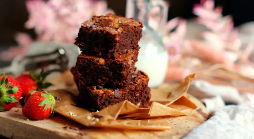 Saftige brownies rezept: Ein Stapel Schokoladenkuchen mit Nüssen, garniert mit frischen Erdbeeren und einem Krug Milch.