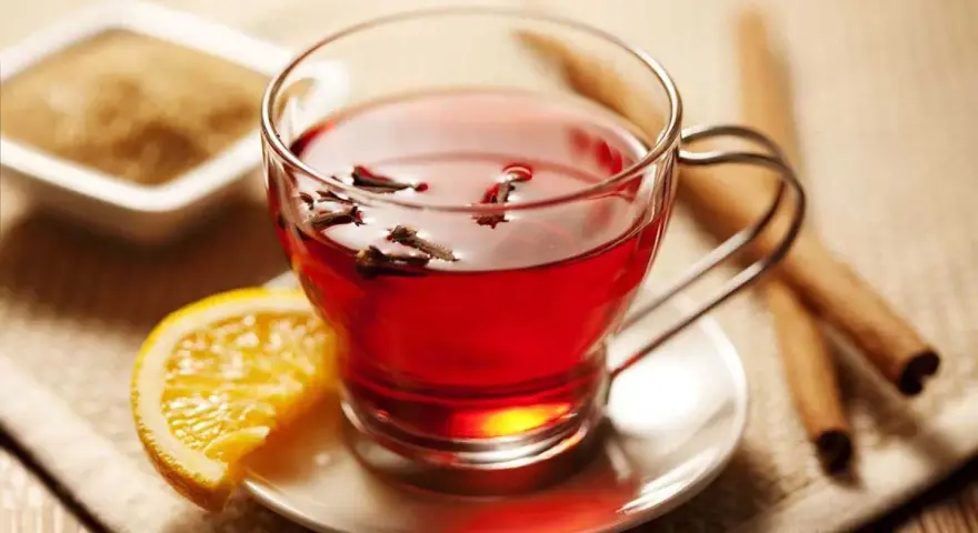 Té rojo con clavo y naranja, ideal para disfrutar de sus propiedades. Azúcar y canela al lado.