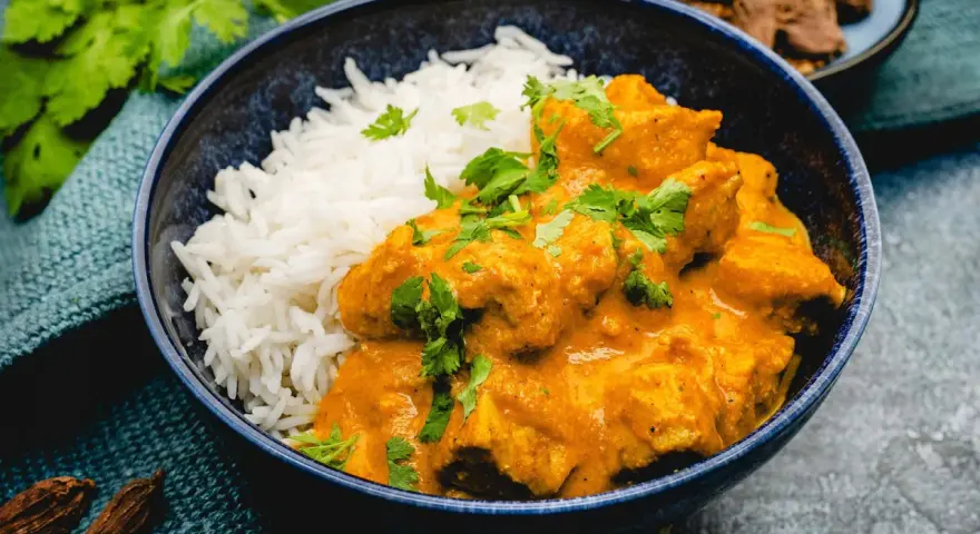 Cremiges Chicken Korma mit Basmatireis, garniert mit frischem Koriander. Ein köstliches indisches Gericht.