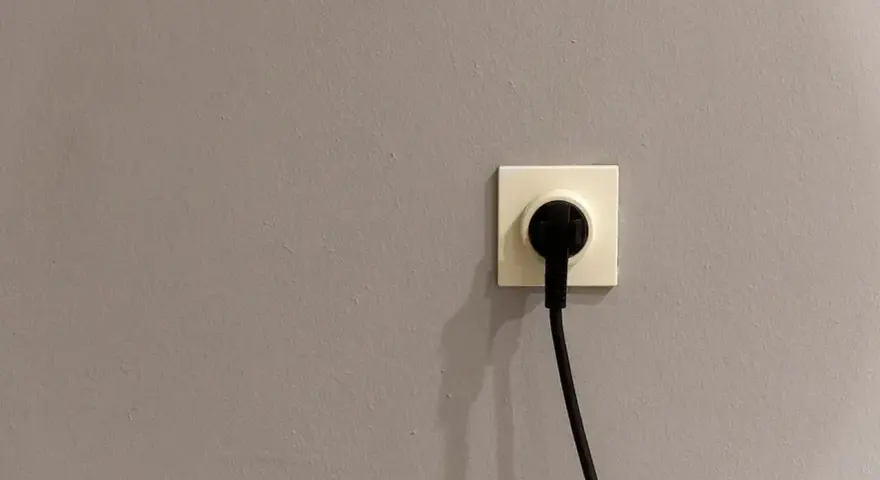 Gniazdko elektryczne z wtyczką na szarej ścianie. Czy to symbol energa taryfa urzędowa?