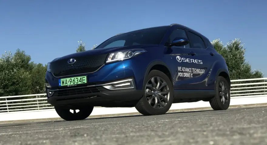 Niebieski SUV Seres 3 zaparkowany na zewnątrz, z widocznym logo i napisem.