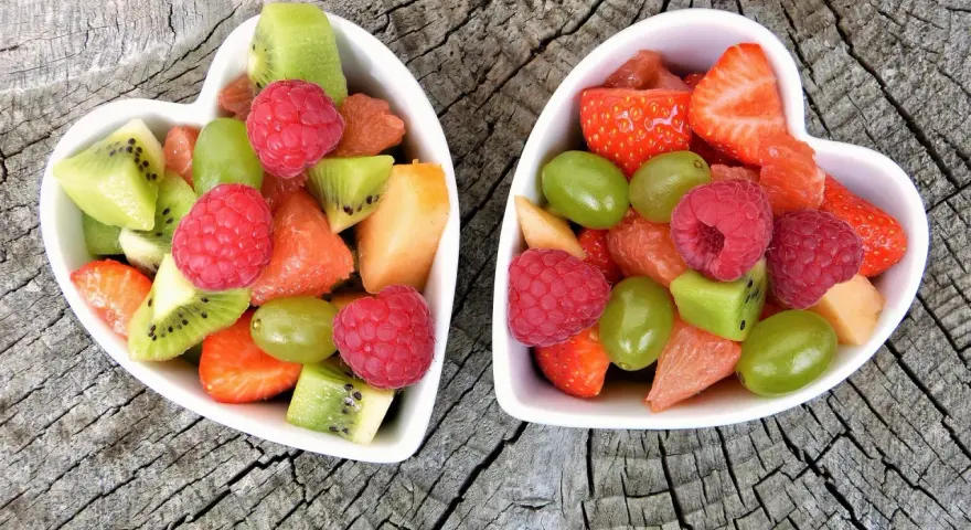 Dwa sercowate talerzyki pełne kolorowych, pokrojonych owoców: truskawek, malin, kiwi, winogron i grejpfruta. Idealne zdrowe przekąski dla dzieci.