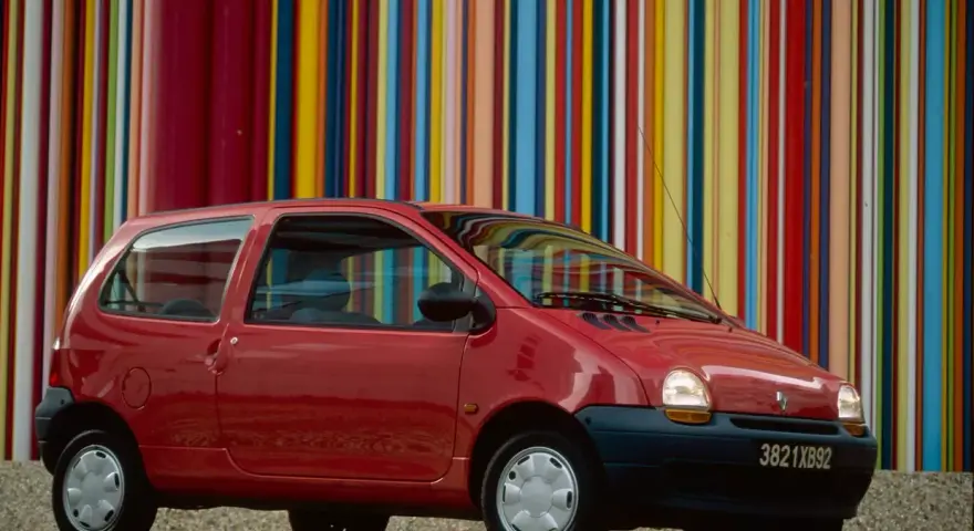 Renault Twingo 1 rouge devant un mur de bandes colorées verticales.