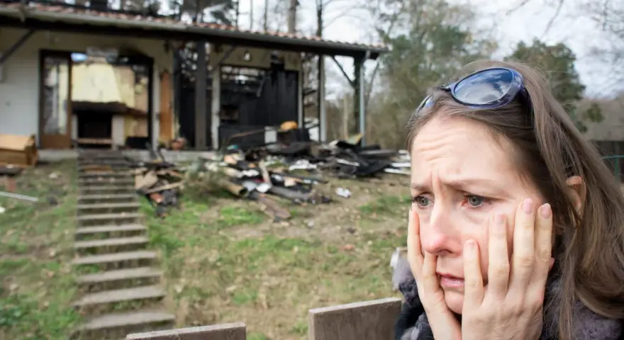 Verzweifelte Frau vor ihrem abgebrannten Haus. Die Versicherung zahlt nicht, ihr Leben liegt in Trümmern.