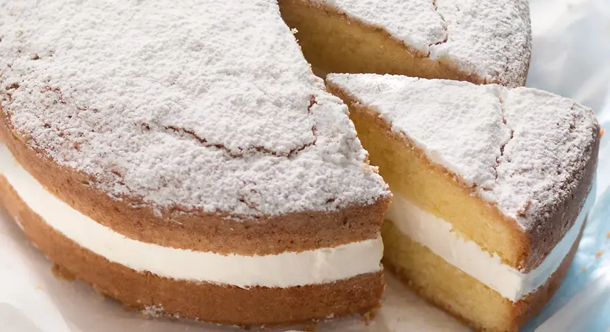 Torta paradiso sofficissima, con crema bianca e zucchero a velo. Una fetta è stata tagliata, invitando a gustarla.