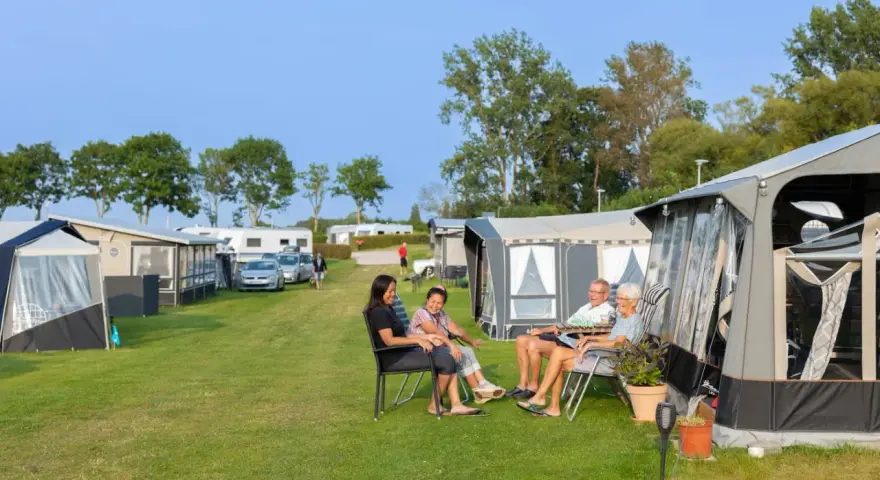 Familj njuter av en solig dag på en av Sveriges billiga campingar. Husvagnar och tält står uppradade på en grön gräsmatta.