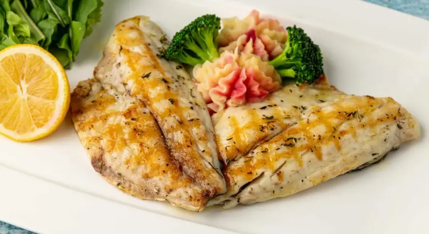 Delicioso gallo a la plancha con puré de patatas rosado, brócoli y rodaja de limón.