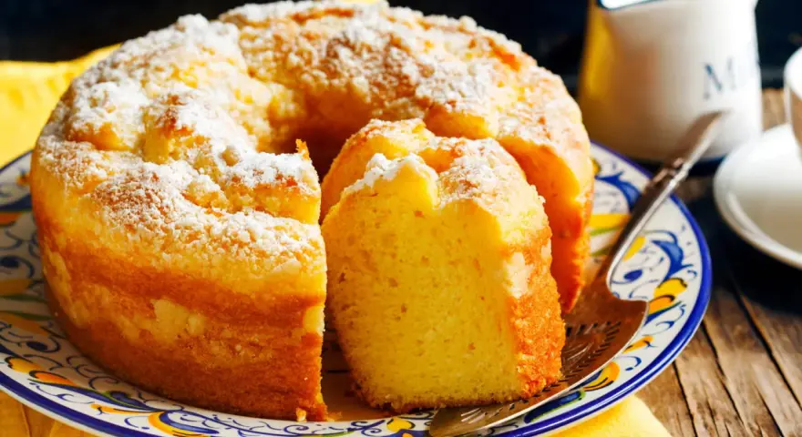 Gâteau sans gluten, saupoudré de sucre glace, sur une assiette décorée. Une part est coupée, prête à être dégustée.