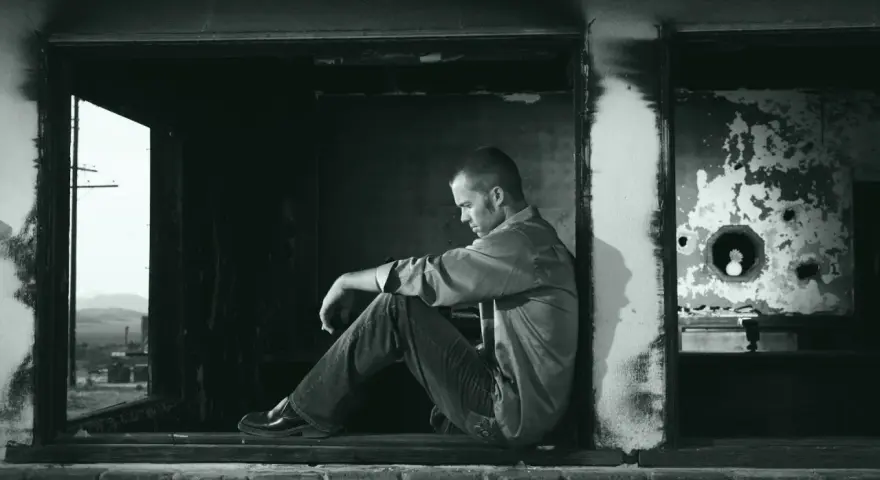 A man sits in a doorway, contemplating what the Bible says about complaining. The scene is stark and desolate, reflecting a mood of introspection.