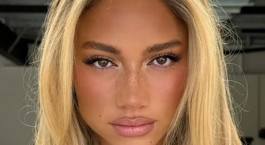 Primer plano de una mujer con cabello rubio y ojos separados, pecas sutiles y labios rosados.