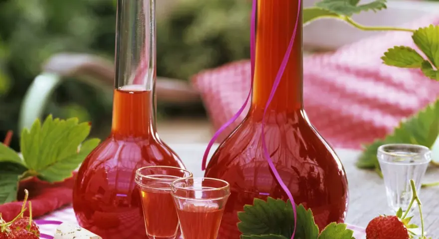 Zwei Flaschen mit rot-orangem Likör, umgeben von Erdbeeren und Blättern. Perfekt, um Erdbeerschnaps selber machen.