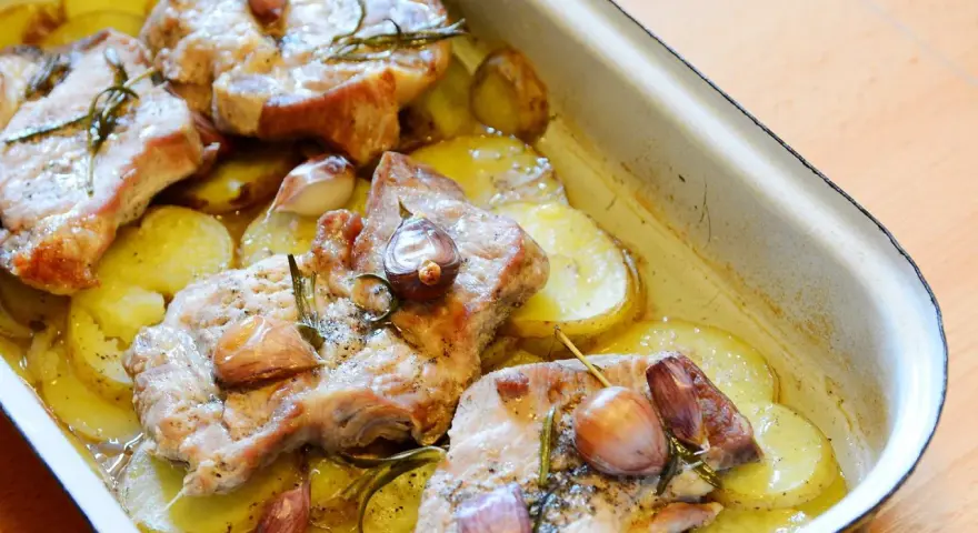 Pieczona karkówka z ziemniakami, czosnkiem i rozmarynem w naczyniu żaroodpornym.