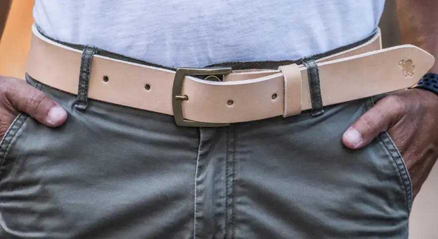 Cintura in cuoio chiaro con fibbia in ottone, indossata su pantaloni verdi. Si vede da che lato si mette la cintura.