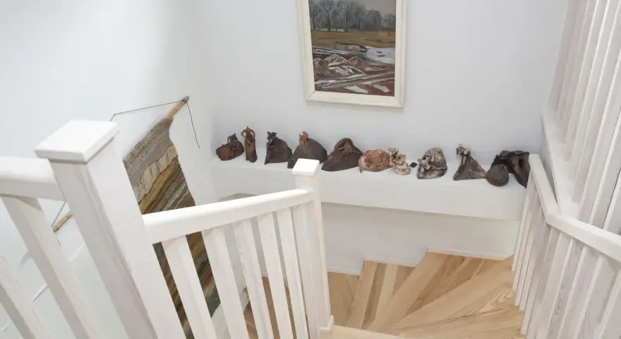 Klatka schodowa inspiracje: białe balustrady, drewniane stopnie i galeria ceramicznych rzeźb na półce.
