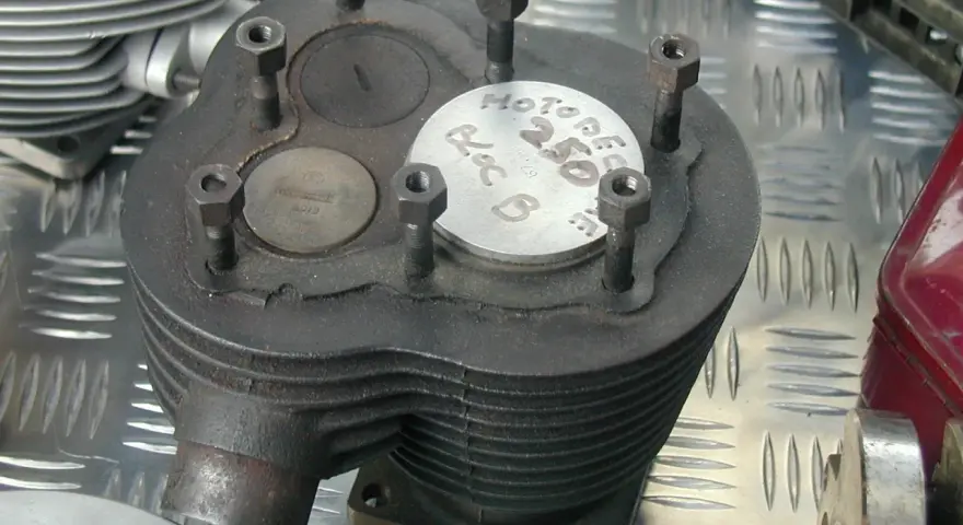 Stary silnik dolnozaworowy z widocznymi zaworami i oznaczeniem "Motobecane 250".