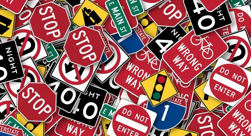 Un groviglio di segnali stradali, tra cui "STOP", "DO NOT ENTER" e "WRONG WAY", che ricordano l'art. 45 del Codice della Strada.