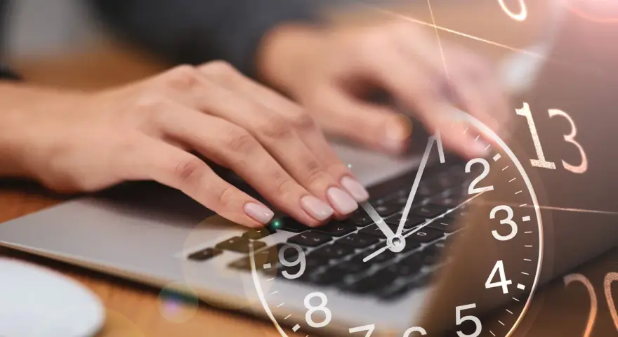 Dłonie piszą na klawiaturze laptopa, a nad nimi unosi się zegar. 13:31 znaczenie - czas na działanie, by osiągnąć cel.