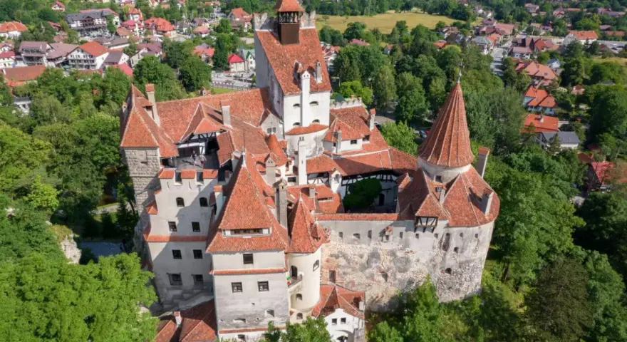 Dracula zamek, majestatyczna twierdza z czerwonymi dachami, otoczona zielenią i malowniczą wioską.