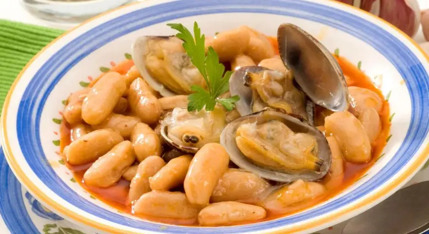 Plato de fabes con almejas, un guiso tradicional asturiano con judías blancas tiernas y jugosas almejas, decorado con perejil fresco.