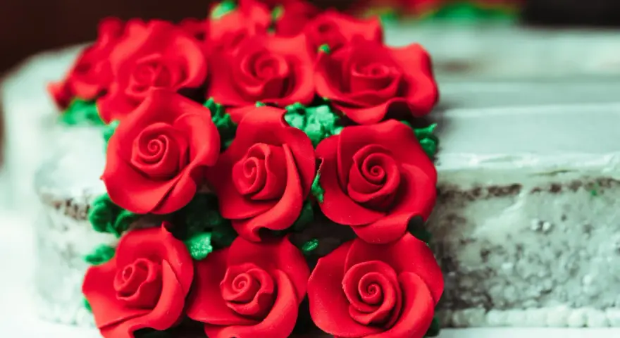 Un mazzo di rose rosse in pasta di zucchero adorna una torta.