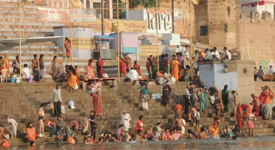 Tłum ludzi w barwnych strojach kąpie się i odpoczywa na schodach nad rzeką Ganges.