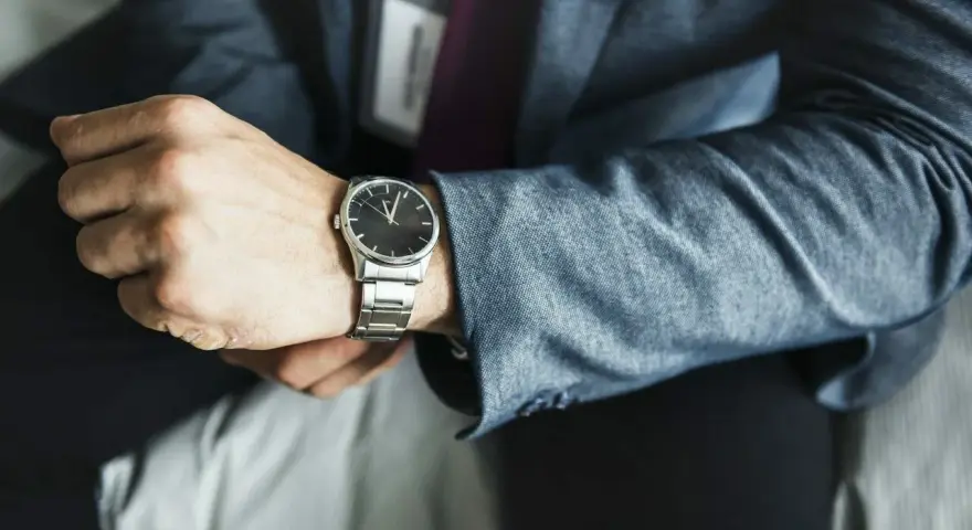 Mężczyzna w garniturze sprawdza czas na zegarku z metalową bransoletą. Może to być moment przed ważnym spotkaniem, wymagającym skracania bransolety w zegarku.