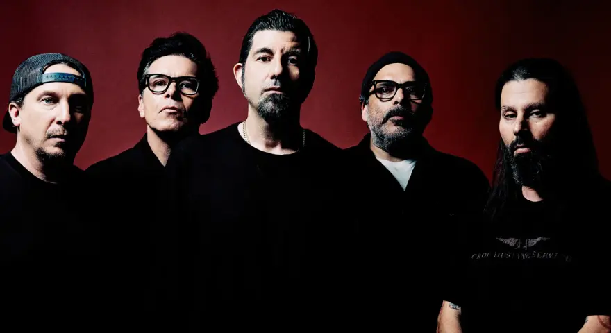 Pięciu mężczyzn, zespół Deftones Polska, pozuje do zdjęcia na ciemnoczerwonym tle.